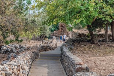 Çift, Alanya Kalesi 'nde taş duvarlar ve yemyeşil yeşilliklerle çevrili manzaralı ahşap bir patika boyunca yürüyor. Barışçıl ortam, tarihi bölgede rahatlatıcı bir gezinti sağlıyor. Alanya, Türkiye - 24 Ekim 2020