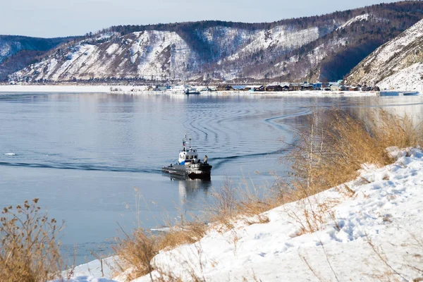 A small boat at the source of the Angara River from Lake Baikal in winter. Baikal port is visible on the opposite bank.