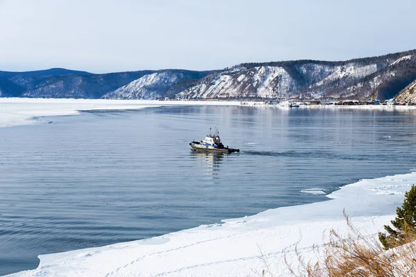 A small boat at the source of the Angara River from Lake Baikal in winter. Baikal port is visible on the opposite bank.