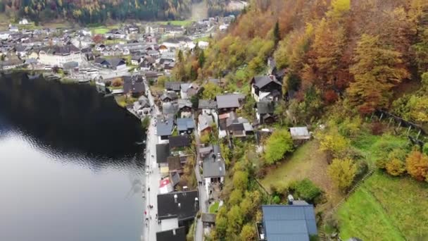 秋天飞越奥地利哈尔斯塔特村上空的无人驾驶飞机 古老的传统住宅和教堂 湖畔和山边覆盖着黄色的秋树 — 图库视频影像