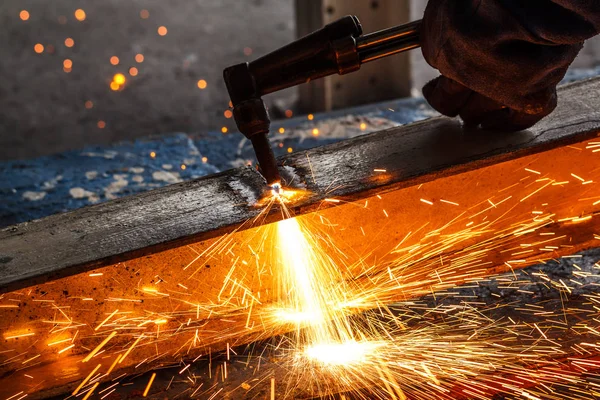 Welder in workshop manufacturing metal construction by cutting to shape using huge orange sparks