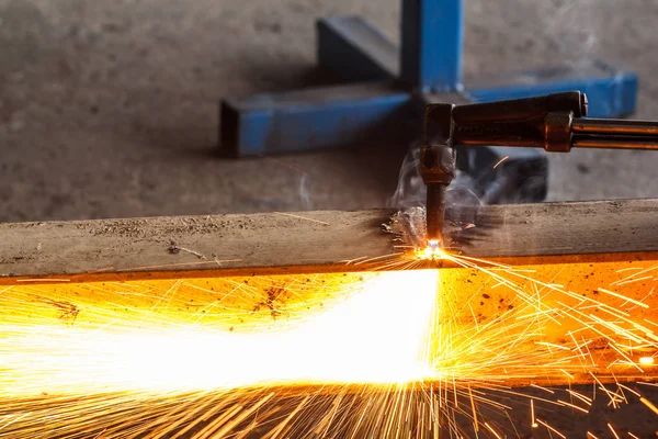 Welder in workshop manufacturing metal construction by cutting to shape using huge orange sparks