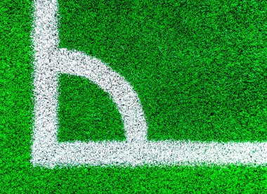 Futbol sahasının köşesinde yeşil çimlerin üzerinde beyaz çizgiler var. 