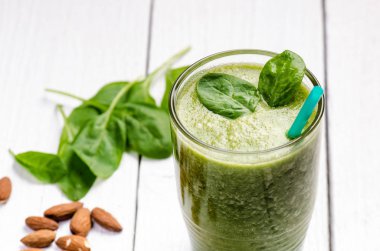 Tahta beyaz arka planda ıspanaklı smoothie. İki yaprak ıspanaklı bir bardak smoothie. Kaçık. Sağlıklı yiyecekler. Kahvaltı..