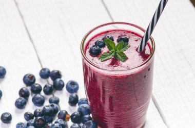 Böğürtlen, ıspanaklı ve portakallı smoothie, ahşap beyaz arka planda. Meyve ve naneli bir bardak smoothie. Böğürtlen, yaprak ve limon, masada ahududu. Meyve, sağlıklı yiyecekler. Kahvaltı..