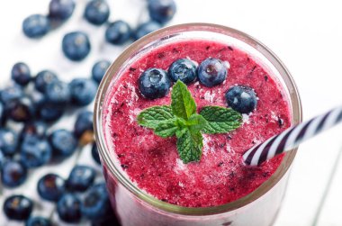 Böğürtlen, ıspanaklı ve portakallı smoothie, ahşap beyaz arka planda. Meyve ve naneli bir bardak smoothie. Böğürtlen, yaprak ve limon, masada ahududu. Meyve, sağlıklı yiyecekler. Kahvaltı..