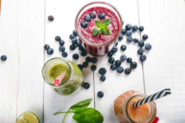 Blueberry, spinachy and orange smoothie on a wooden white background. Glasses of smoothie with berry and mint. Berry, leaf and lime, raspberries on a table. Fruit Healthy food. Breakfast.