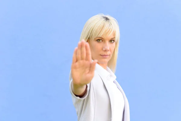 Stern young woman making a stop gesture with her raised hand as she stands outdoors with focus to her face and copy space