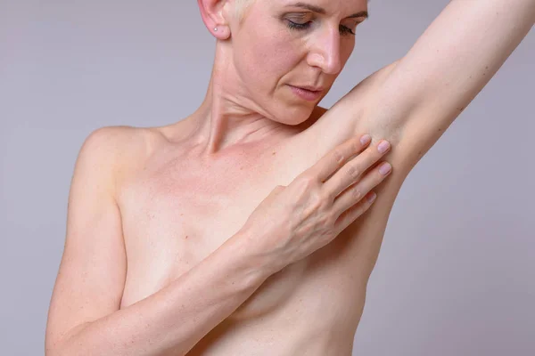 Middleaged woman checking the lymph nodes under her arm for lumps during her routine check of her breast for signs of early cancer