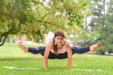 Onun ellerine sağlık ve fitness kavramı kamerada gülümseyen hava uzanmış bacaklar ile dengeleme bir parkta çalışma dışarı güçlü esnek kadın