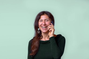 Yeşil arka plana karşı cep telefonunda bahseden neşeli olgun kadın portresi