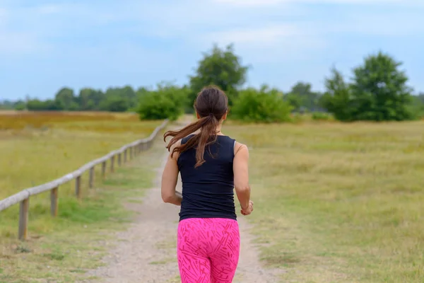 Female adult jogger running away from camera along unpaved road in a close up view