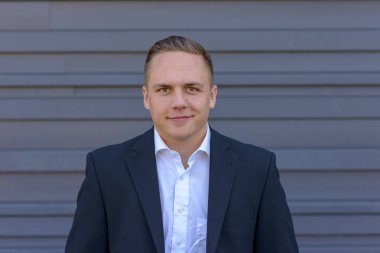 Çekici genç iş adamı ile küçük bir gülümseme bir açık boyun gömlek ve takım elbise ceket ayakta gri bir duvar önünde