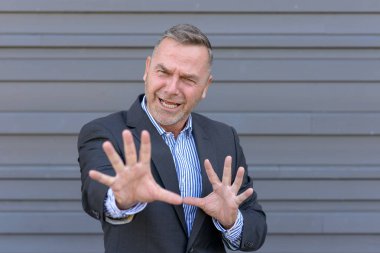 Bir şeyler onun önünde kopya alanı ile gri bir duvara genişletilmiş elleriyle fending şık orta yaşlı işadamı