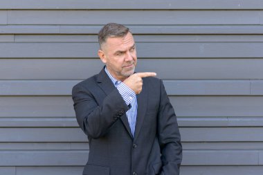 Suçu ya da bir şey kopya alanı gri bir duvarla karşı ciddi bir ifade ile belirlemek için yan parmakla işadamı