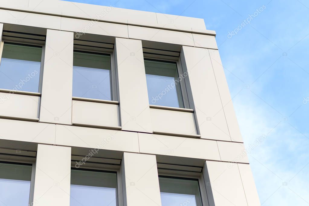 Side view of tall building with rectangular windows reflecting bright blue sky with very thin clouds