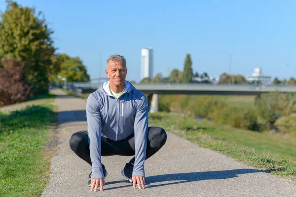 Średnim Wieku Runner Siedzi Squat Rękami Ziemi — Zdjęcie stockowe