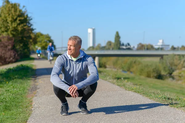 Middle aged runner sitting in a squat while taking a break and looking to the side