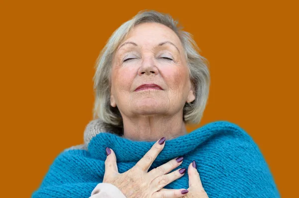 Attractive senior woman savoring the moment standing with her eyes closed and head tilted back with a serene expression as she clasps her chest with her hands