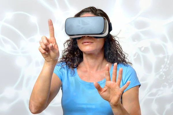 Woman experiencing a virtual environment as she watches the simulated graphics on a pair of virtual reality glasses with a serious expression pointing upwards