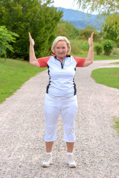 Sporty elderly woman doing sport exercises raising both arms up