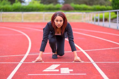 Conceptual image of a businesswoman on a race track in the ready position on the starting line facing towards the camera clipart