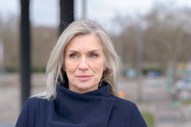 Dalgın çekici kadın portre yakından kasabasında açık bir kaldırım üzerinde duruyor gibi kameranın sessiz bir gülümseme ile ÜEP omuz uzunluk sarışın saçlı