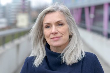 O şehirde bir açık yaya geçidi üzerinde duruyor gibi güzel bir gülümseme ile Güzel doğal gri sarışın orta yaşlı kadın objektife bakıyor