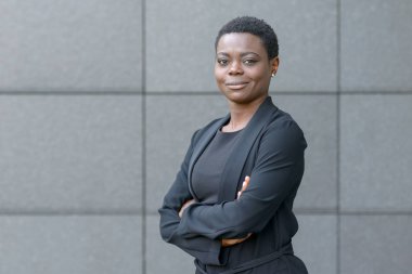 Kendine güvenen dostu genç profesyonel Afrikalı kadın katlanmış silah ve yan kopya alanı ile gri taştan bir duvar önünde poz sessiz bir gülümseme ile