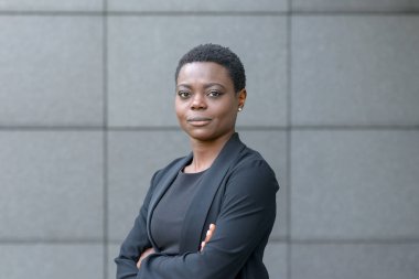 Kendine güvenen dostu genç profesyonel Afrikalı kadın katlanmış silah ve yan kopya alanı ile gri taştan bir duvar önünde poz sessiz bir gülümseme ile