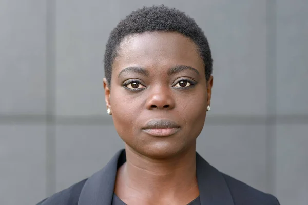 Front bust portrait of beautiful black woman with short haircut, wearing black business clothes and small earrings. Looking at camera with calm face