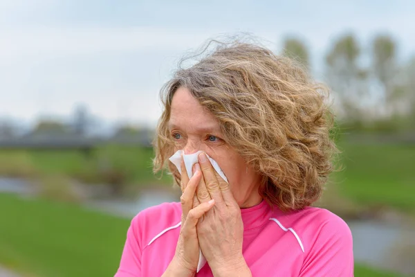 Woman outdoors blowing nose in napkin — Stock Photo, Image