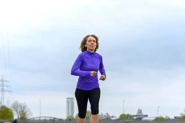 Ajuste mujer activa corriendo contra un cielo nublado — Foto de Stock