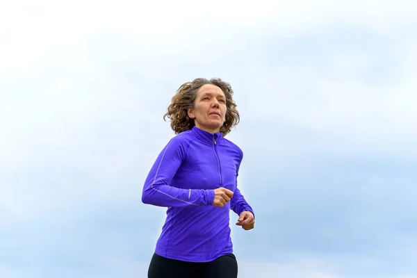 Ajuste mujer activa corriendo contra un cielo nublado — Foto de Stock