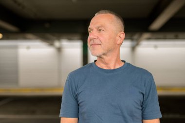 Kısa gri saçlı, sakallı ve mavi tişörtlü kendinden emin yaşlı bir adam.