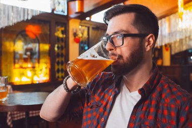 Gözlüklü genç bir adam yakın plan bir barda bira içiyor..