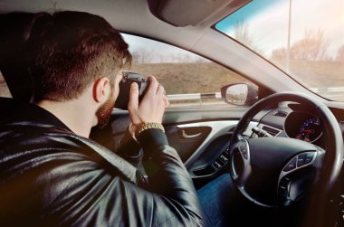 Fotoğrafçı bir araba kullanıyor. Bir fotoğraf makinesi ile güzel adam. Araba fotoğrafları inceliyor. Pencereden seyahat fotoğrafları