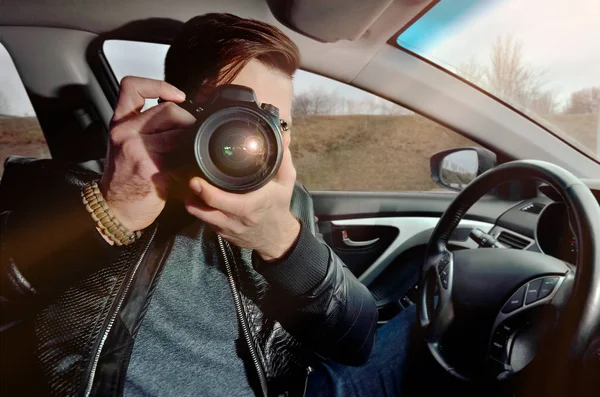 The photographer is driving a car. Beautiful guy with a photo camera. Examines photos in the car. The traveler photographs through the window
