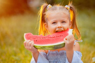 Küçük kız gün batımı ışınları yeşil bir çim üzerinde karpuz bir dilim ısırır