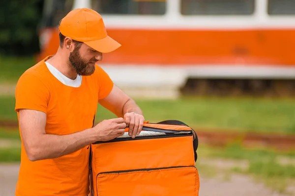 Food delivery man in orange uniform opens a food delivery bag.