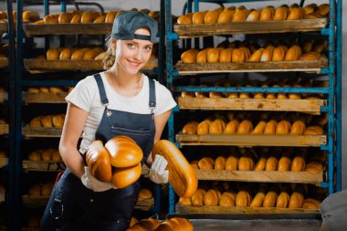 Fırıncı kız, fırının arka planındaki fırından ekmek ile birlikte sıcak ekmek alıyor. Sanayi ekmek üretimi. Bir fırında otomatik hat