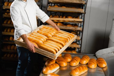 Fırıncı, rafların arkasında sıcak ekmek ve fırında ekmek olan ahşap bir kutu tutuyor. Sanayi ekmek üretimi