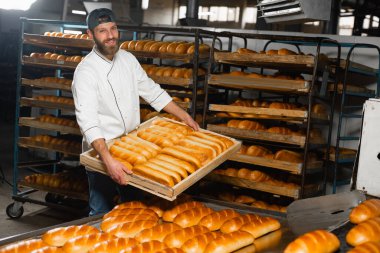 Fırıncı, rafların arkasında sıcak ekmek ve fırında ekmek olan ahşap bir kutu tutuyor. Sanayi ekmek üretimi
