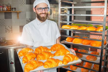 Genç yakışıklı fırıncı fırının arka planında taze kruvasan tutuyor..