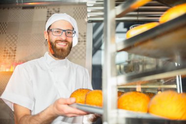 Genç ve yakışıklı bir fırıncı fırından taze fırın çıkarır..