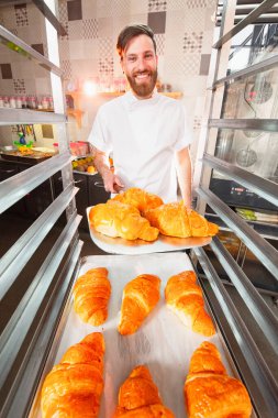Genç ve yakışıklı bir fırıncı elinde taze kruvasanlar tutuyor..