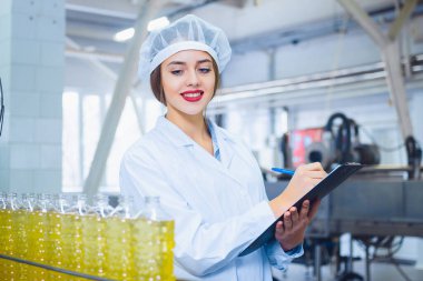Güneş çiçeği ve zeytinyağı üretimi için bir fabrikada elinde tabletle beyaz tulumlu güzel bir kız. Üretimde kalite kontrolü