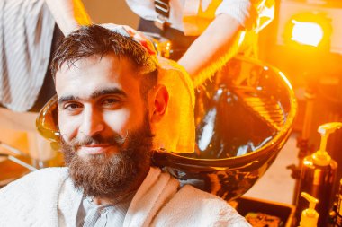 Berber, lavaboda sakallı ve bıyıklı genç yakışıklı bir adamın kafasını yıkıyor. Erkek Güzellik Salonu.