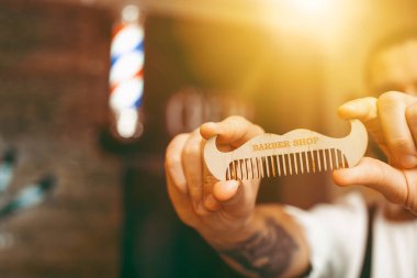 Elinde bıyık şeklinde bir tarak olan yakışıklı, sakallı genç bir berber. Berber dükkanı. Boşluğu kopyala