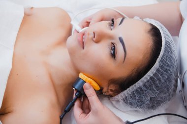 Cilt bakımı. Mikro akım terapisi. Cilt bakımı prosedürleri ile ilgilenen güzel bir genç kız. Donanım kozmetolojisi. Kaplıcadaki yüz derisi temizleniyor.